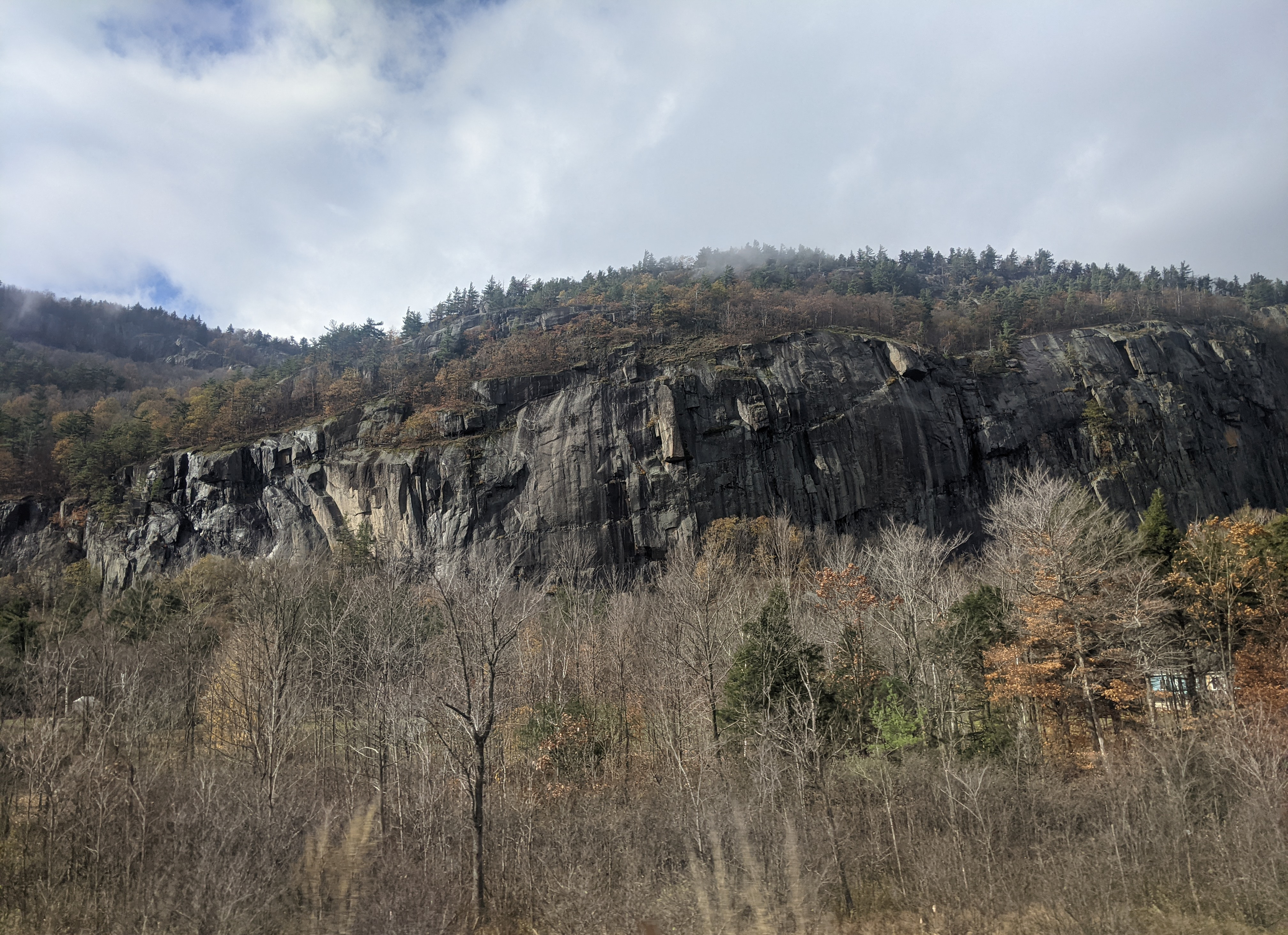 A sheer, rocky cliff face, viewed from a road.