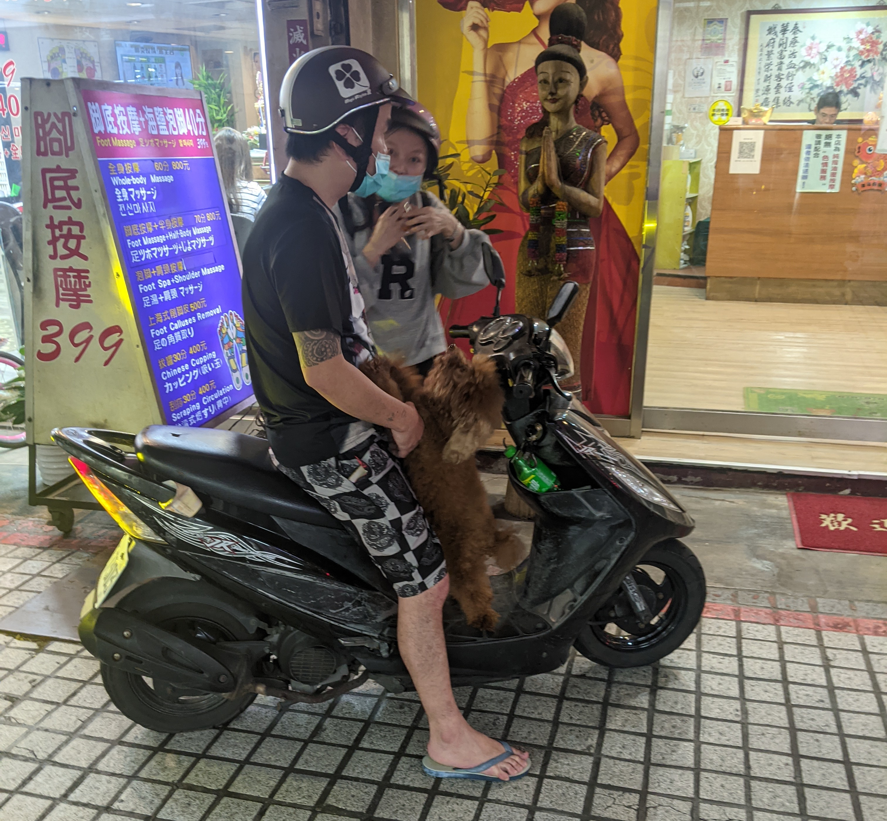 A dog standing at the feet of someone riding a scooter.