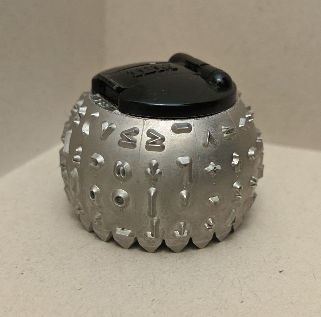 A metal semi-sphere with characters embossed onto it, including mathematical symbols and shapes.
